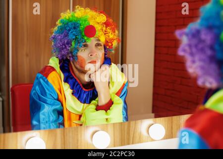 Le clown du cirque regarde dans un miroir dans une salle de maquillage. En attente du divertissement. Banque D'Images