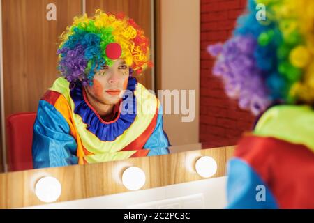 Le clown du cirque regarde dans un miroir dans une salle de maquillage. En attente du divertissement. Banque D'Images