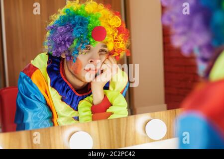 Le clown du cirque regarde dans un miroir dans une salle de maquillage. En attente du divertissement. Banque D'Images