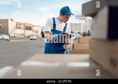 Livreur en colis de contrôle uniforme, service de livraison. Homme debout sur des emballages en carton dans le véhicule, livraison mâle, messagerie ou expédition Banque D'Images