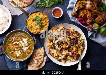 Dîner de cuisine indienne : poulet tandoori, biryani, lentille rouge curry dal avec riz naan, paneer palak et riz basmati sur fond de béton foncé Banque D'Images