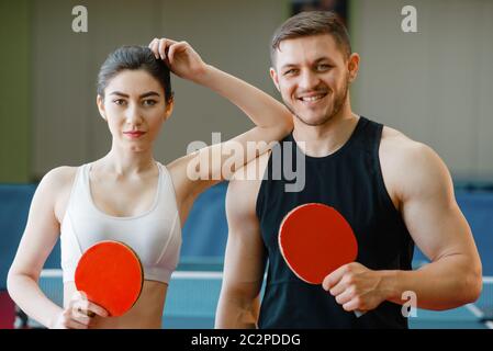 L'homme et la femme est titulaire des raquettes de ping-pong à l'intérieur. Couple in sportswear joue au tennis de table dans une salle de sport. Hommes et des femmes dans un club de tennis de table Banque D'Images