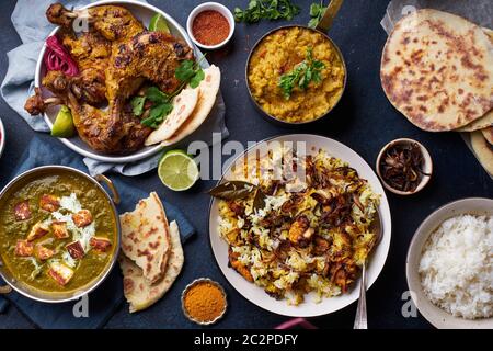 Dîner de cuisine indienne : poulet tandoori, biryani, lentille rouge curry dal avec riz naan, paneer palak et riz basmati sur fond de béton foncé Banque D'Images