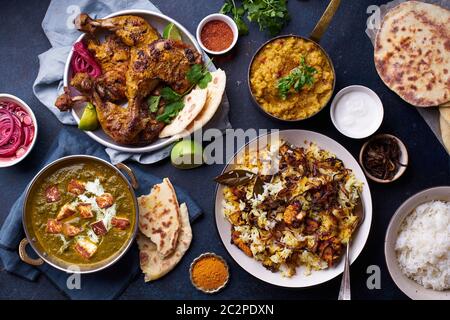 Dîner de cuisine indienne : poulet tandoori, biryani, lentille rouge curry dal avec riz naan, paneer palak et riz basmati sur fond de béton foncé Banque D'Images