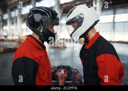 Deux kart coureurs dans des casques debout face à face, karting auto sport intérieur. Course de vitesse sur une piste de karting étroite avec barrière pour pneus. Véhicule rapide de la marque Banque D'Images