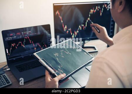 Investisseur homme analysant le graphique du marché boursier en utilisant un stylo pointant vers l'écran d'ordinateur. Banque D'Images