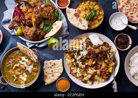 Dîner de cuisine indienne : poulet tandoori, biryani, lentille rouge curry dal avec riz naan, paneer palak et riz basmati. Vue de dessus sur le fond en béton foncé Banque D'Images