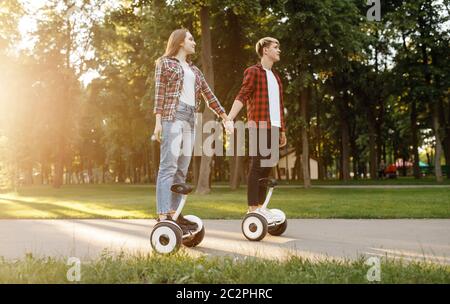 Jeune couple riding sur le gyroscope conseil en parc d'été au coucher du soleil. Loisirs de plein air avec gyroboard électrique. Transport avec la technologie de l'équilibre, de l'électricité Banque D'Images