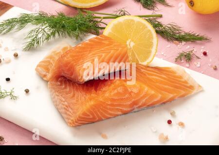 Tranches de saumon au citron et aneth, close-up avec sel et poivre, la cuisson du poisson, sur un fond rose Banque D'Images