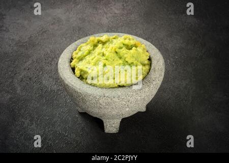 Le guacamole dans un molcajete, avocat mexicain dans la mortier traditionnel en pierre, sur un fond noir Banque D'Images