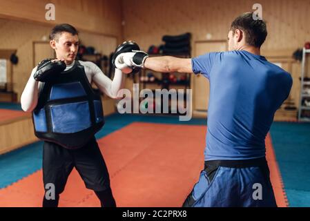 Dans kickboxer mâles pratiquant gants poinçon manuel avec un entraîneur personnel dans la région de pads, de l'exercice dans la salle de sport. Boxer sur la formation, la pratique de kickboxing Banque D'Images