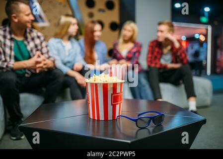 Un groupe d'adolescents se détendent sur le canapé et attendent le spectacle dans le hall de cinéma. Les jeunes hommes et femmes sont assis sur un canapé dans le cinéma, pop-corn sur le Banque D'Images