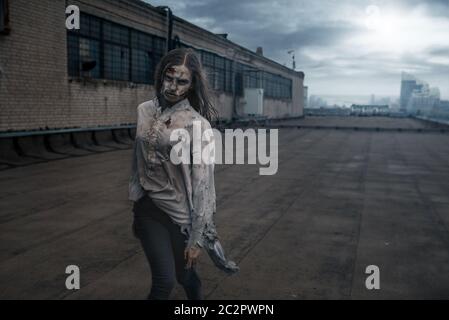 Zombie féminin effrayant sur le toit d'un bâtiment abandonné, poursuite mortelle. Horreur en ville, attaque de craies effrayantes, apocalypse Banque D'Images