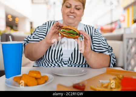 Fat Woman eating fast food mall en cour. L'excès de personne de sexe féminin à la table avec l'ordure le déjeuner Banque D'Images