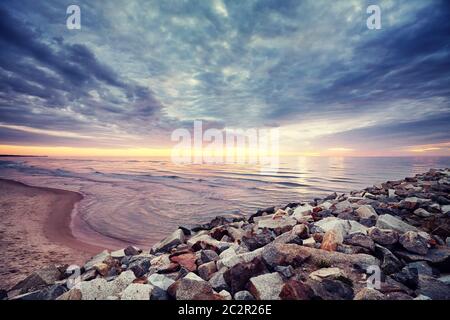Jetée rocheuse avec ciel spectaculaire au coucher du soleil, couleurs vives appliquées. Banque D'Images