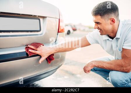 Polissage extérieur voiture sur la station de lavage. L'homme frotte pare-choc du véhicule automobile avec polish Banque D'Images