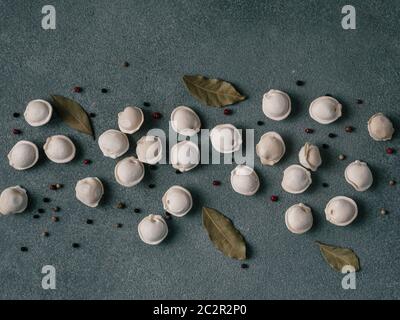 Schéma des pelmeni russes non cuits congelés avec des grains de poivre et les feuilles de laurier sur fond noir. Mise en page créative de boulettes. Belles matières épars Banque D'Images