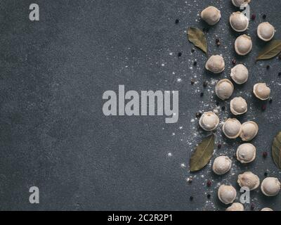 Schéma des pelmeni russes non cuits congelés avec des grains de poivre et les feuilles de laurier sur fond noir. Mise en page créative de boulettes. Belles matières épars Banque D'Images