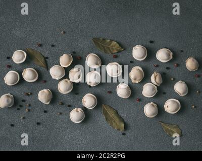 Schéma des pelmeni russes non cuits congelés avec des grains de poivre et les feuilles de laurier sur fond noir. Mise en page créative de boulettes. Belles matières épars Banque D'Images