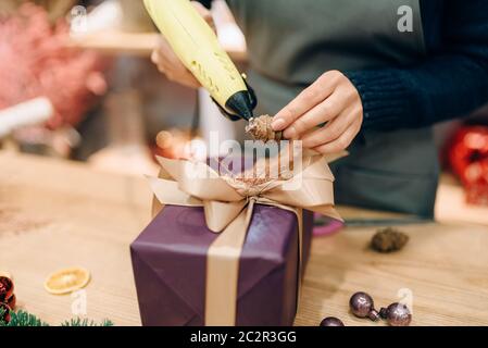 Vendeur femelle décore boîte-cadeau avec fir cone, handmade rétractable et la décoration. Femme wraps présent sur la table, le décor intérieur Banque D'Images