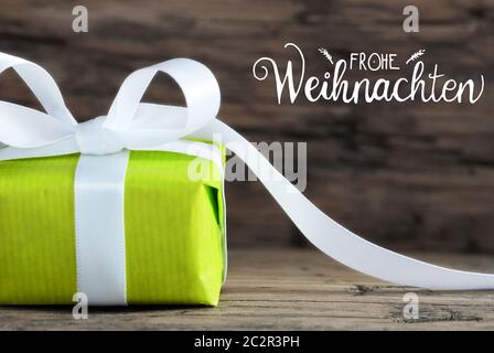 L'étiquette avec la calligraphie allemand Frohe Weihnachten signifie joyeux Noël. Un cadeau vert avec arc blanc. Fond en bois brun Banque D'Images
