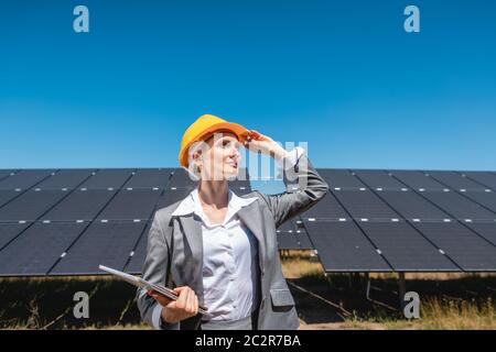Femme d'affaires ou investisseur inspectant sa ferme solaire debout devant des panneaux photovoltaïques Banque D'Images