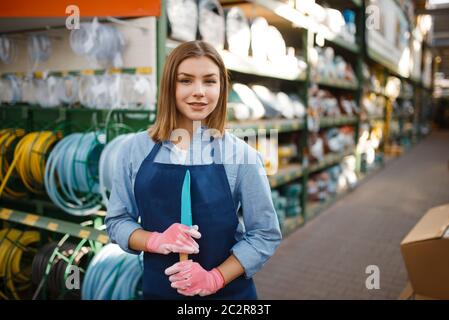 Jardinier féminin en tablier et gants en magasin pour le jardinage. Femme vend du matériel en magasin pour la floriculture, vente d'instruments de fleuriste Banque D'Images