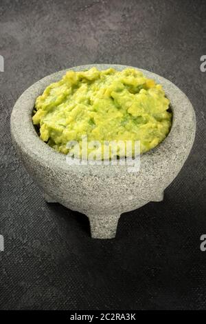 Le guacamole dans un molcajete, avocat mexicain sauce trempette dans le mortier traditionnel en pierre, sur un fond noir avec une place pour le texte Banque D'Images