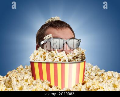 Homme dans des verres dans un seau de pop-corn contre le bleu Banque D'Images