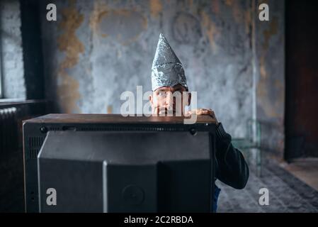 Homme peur en aluminium bouchon regarder la TV, protection de l'esprit, concept de paranoïa. OVNI, théorie du complot, phobie de la télépathie Banque D'Images