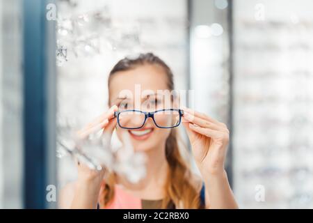 Femme étant satisfaite des nouvelles lunettes qu'elle a achetées dans le magasin les tenant devant son visage Banque D'Images