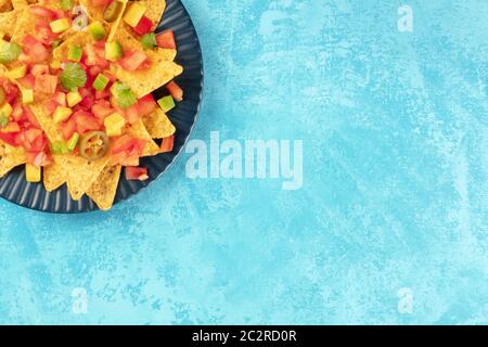 Nachos mexicains en gros plan, chips de tortilla avec des feuilles de tomate, d'avocat et de coriandre, surfilé sur un backgroun tuquoise vibrant Banque D'Images