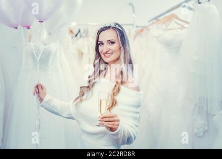 Mariée à être en blanc avec des ballons dans la boutique de vêtements de mariée toasting avec un verre de champagne Banque D'Images