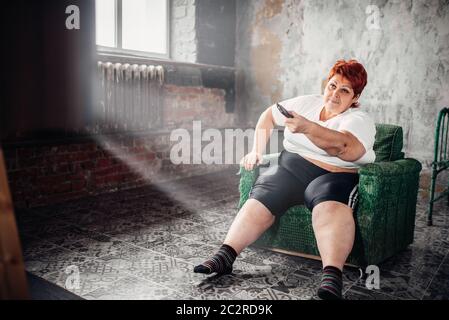 L'excès de femme assise dans un fauteuil et regarde la télévision. Mode de vie malsain, l'obésité Banque D'Images