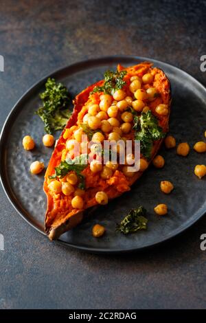 Patate douce cuite farcie de pois chiches et de chou frisé sur une assiette noire. Plat végétarien savoureux pour le dîner ou le déjeuner. Banque D'Images