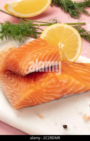 Tranches de saumon au citron et aneth, close-up avec sel et poivre, la cuisson du poisson, sur un fond rose Banque D'Images