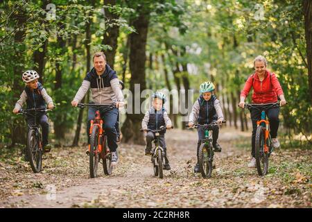 parents et enfants en vélo sur le sentier forestier. Jeune famille dans des vêtements chauds en vélo dans le parc d'automne. Vélo de montagne familial sur la forêt. Banque D'Images