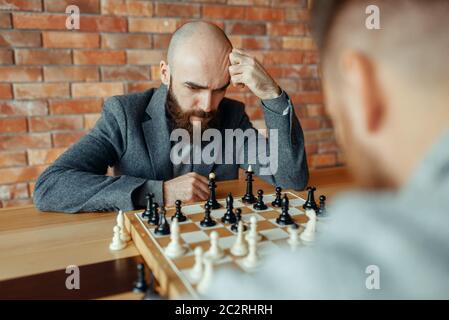 Les joueurs d'échecs à l'homme, processus de réflexion. Deux chessplayers commencer le tournoi intellectuelle à l'intérieur. Sur l'Échiquier, jeu de stratégie, table en bois Banque D'Images