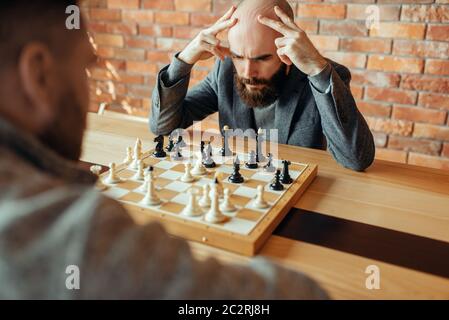 Les joueurs d'échecs à l'homme, processus de réflexion. Deux chessplayers commencer le tournoi intellectuelle à l'intérieur. Sur l'Échiquier, jeu de stratégie, table en bois Banque D'Images