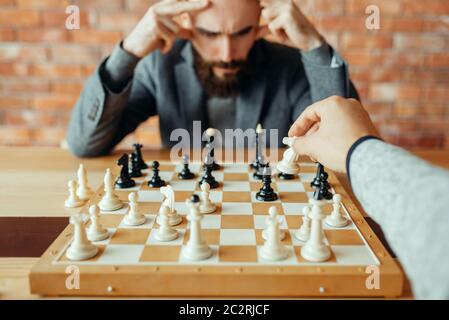 Les joueurs d'échecs masculins jouent à bord, le chevalier blanc se déplace. Deux joueurs de chessPlayers commencent le tournoi intellectuel à l'intérieur. Échiquier sur table en bois Banque D'Images