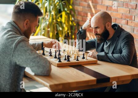 Les joueurs d'échecs à jouer à bord, déplacer l'éléphant noir. Deux chessplayers commencer le tournoi intellectuelle à l'intérieur. Sur l'échiquier table en bois Banque D'Images