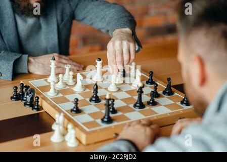 Les joueurs d'échecs à l'homme, processus de réflexion. Deux chessplayers commencer le tournoi intellectuelle à l'intérieur. Sur l'Échiquier, jeu de stratégie, table en bois Banque D'Images