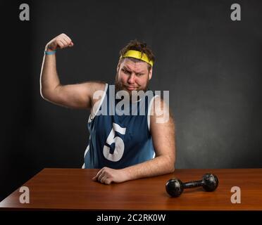 Fat Man montre ses muscles avec un haltère à la table Banque D'Images