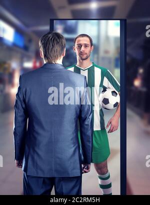 Un homme d'affaires rêvant d'être un joueur de football se tient devant le miroir Banque D'Images