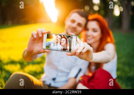 Love couple fait sur téléphone appareil selfies en parc d'été sur le coucher du soleil. Date romantique de jolie femme et jeune homme Banque D'Images