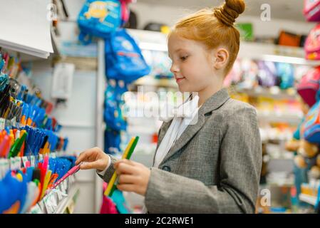 École fille choisissant un stylo à l'étagère dans le magasin de papeterie. Une femme achète des fournitures de bureau dans un magasin, une écolière dans un supermarché Banque D'Images