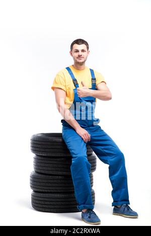 Conscrit dans l'uniforme bleu assis sur pneumatiques, fond blanc, réparateur de pneus Banque D'Images