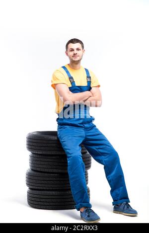 Conscrit dans l'uniforme bleu assis sur pneumatiques, fond blanc, réparateur de pneus Banque D'Images