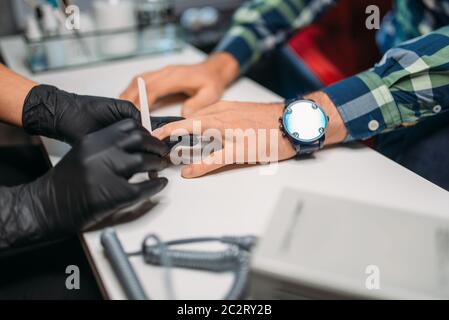 Dans la beauté des ongles polissage gants noirs aux clients masculins, vue du dessus, les hommes à salon de manucure. Procédure de soins des mains manucure faisant Banque D'Images