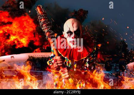 Crazy clown sanglant avec batte de baseball, avion en feu sur l'arrière-plan. Homme avec un miroir en costume halloween effrayant, killer Banque D'Images